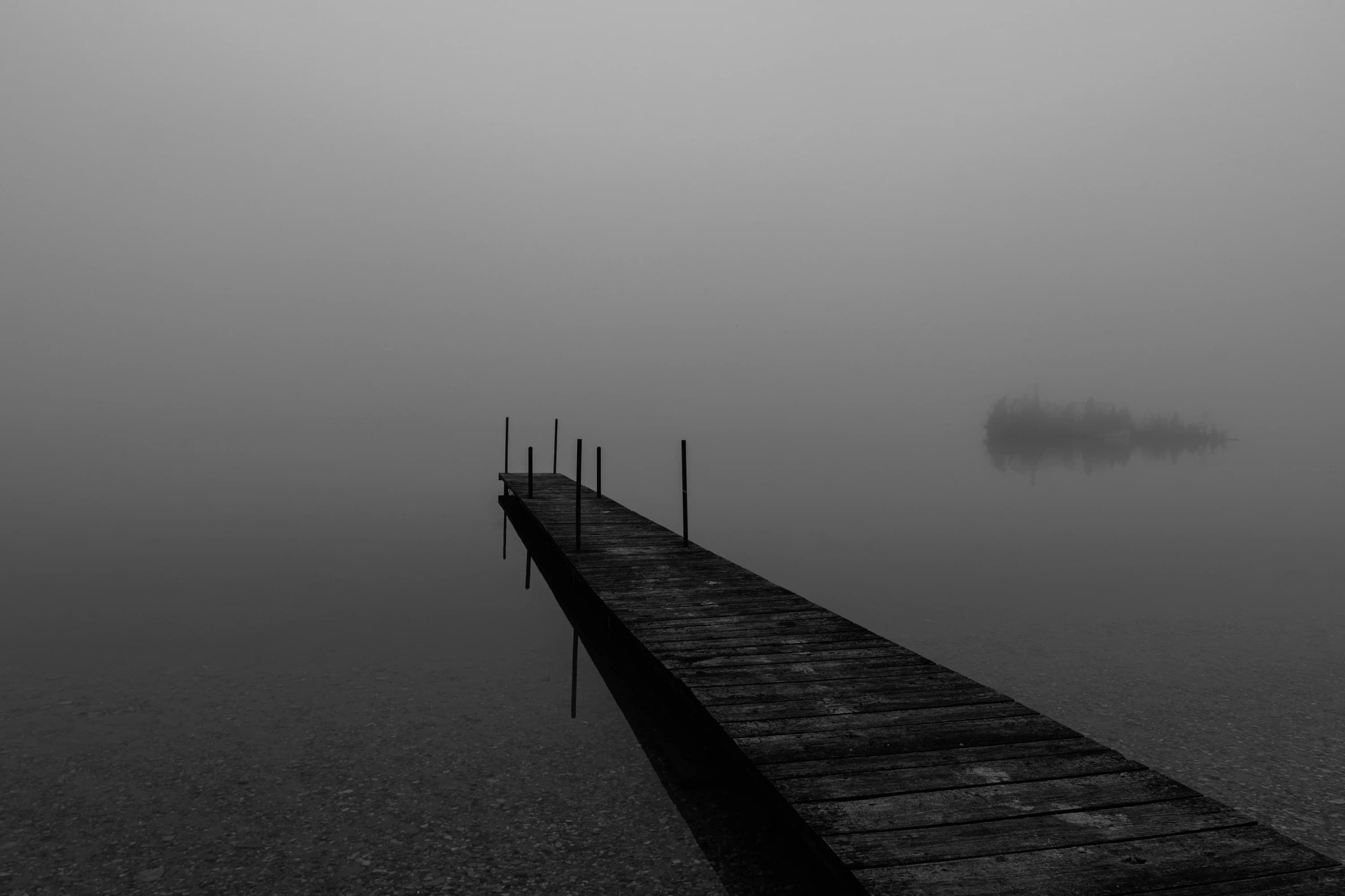 A dock extending over water in dense fog.